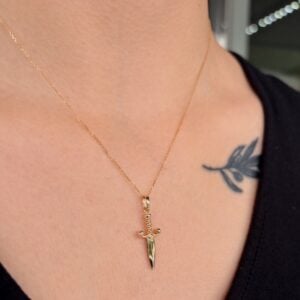 Gold chain necklace with a small dagger pendant resting on the collarbone