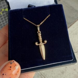 Gold sword pendant on a delicate chain resting in a navy velvet jewelry box, ready as a gift piece
