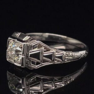 Diamond engagement ring in a white metal with a geometric stepped side design and a central round diamond setting.