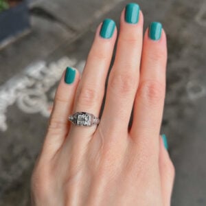 Close-up of a left hand with turquoise nails, wearing a silver diamond engagement ring on the ring finger.